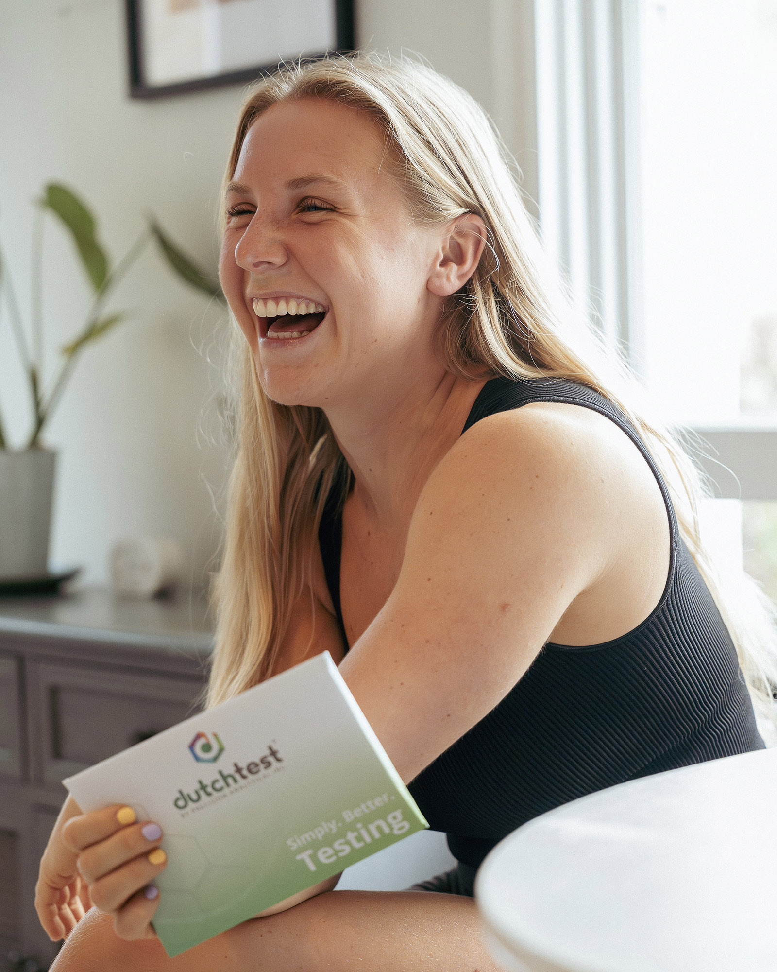 Smiling Gigi holding a DUTCH hormone test kit during functional hormone testing consultation